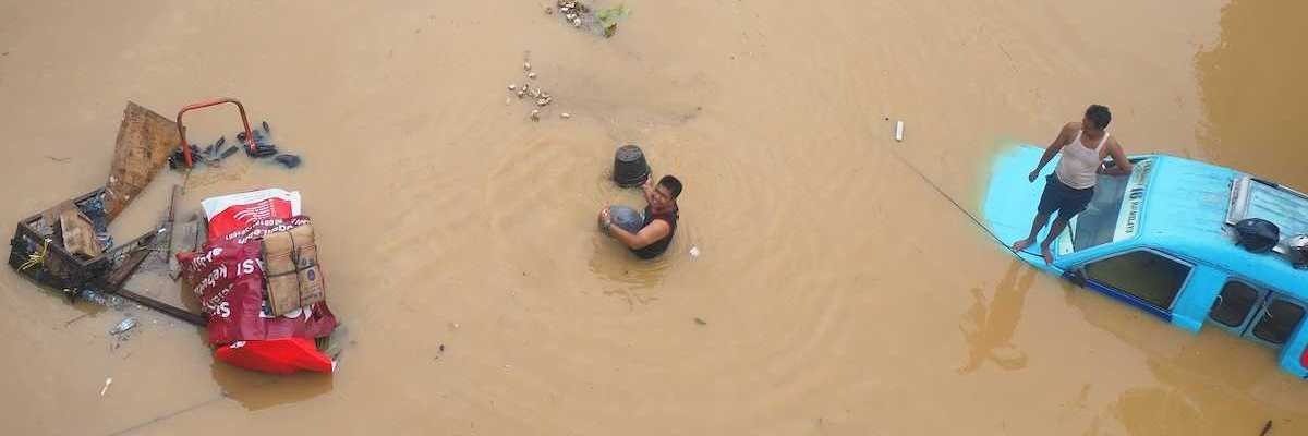 Two men attempting to salvage items inundated by floodwaters amidst submerged vehicles.