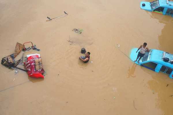 Two men attempting to salvage items inundated by floodwaters amidst submerged vehicles.