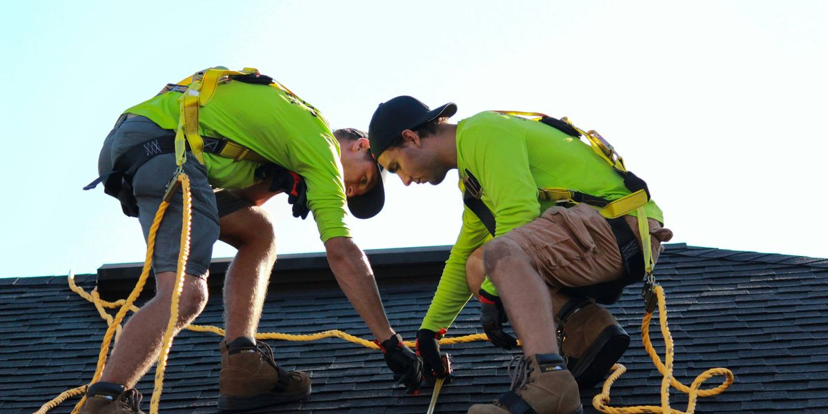 Two men holding rope and setting up a roof for solar panels.
