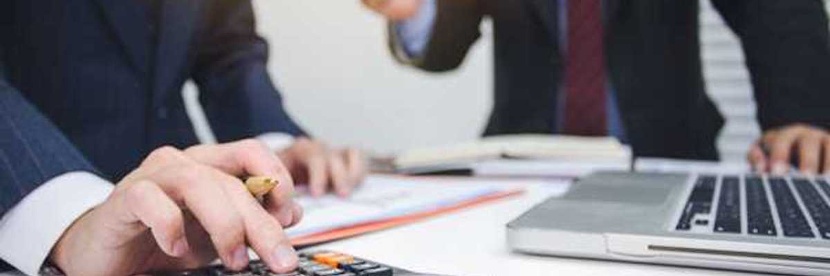 Two men in suits tallying numbers on a calculator