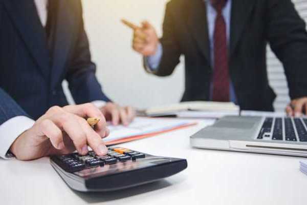 Two men in suits tallying numbers on a calculator