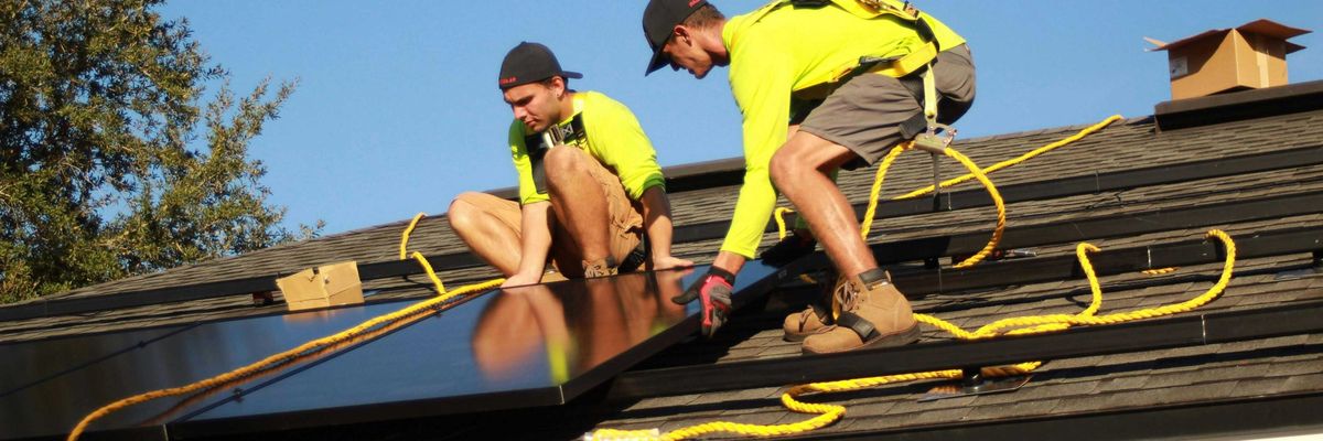 Two men installing solar panels on a roof.