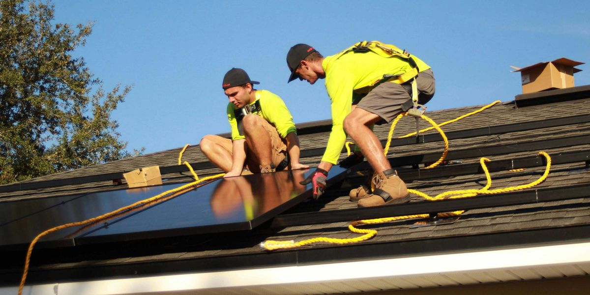 Two men installing solar panels on a roof.
