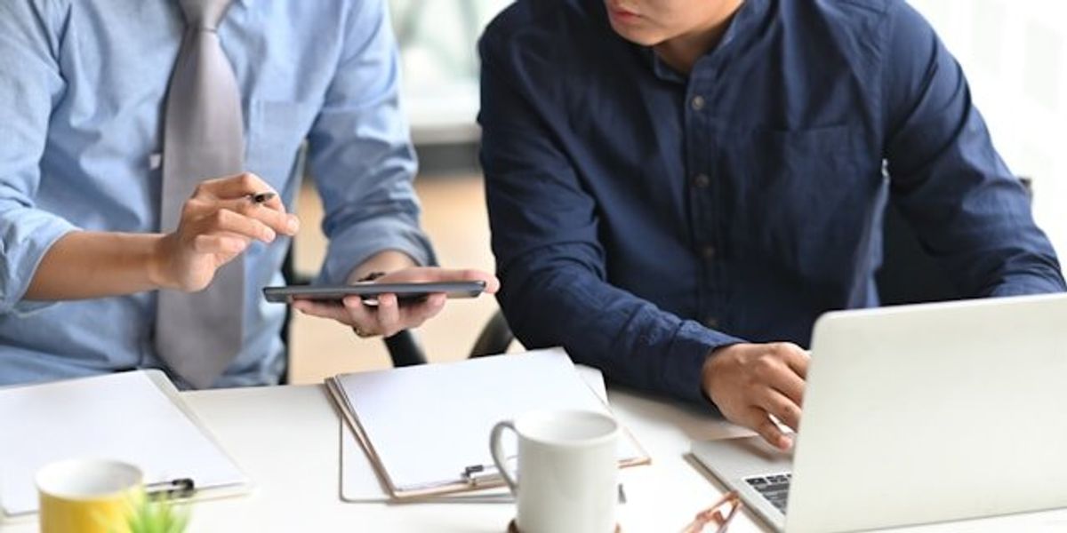 Two men looking at a tablet while working at a computer