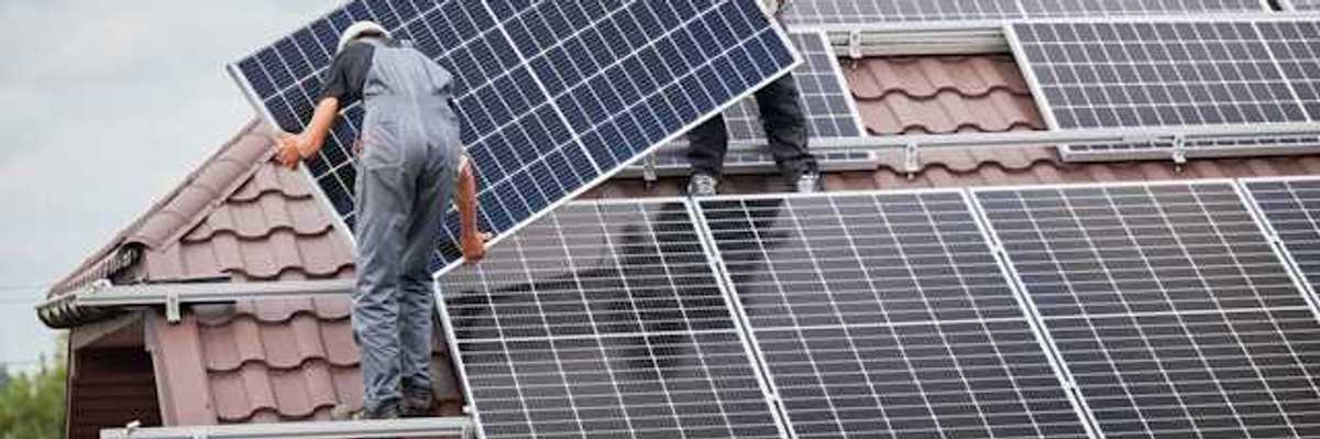 Two men on a roof with overalls on installing a solar panel