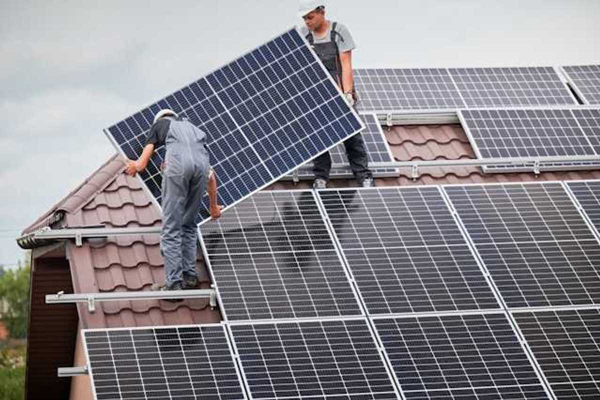 Two men on a roof with overalls on installing a solar panel
