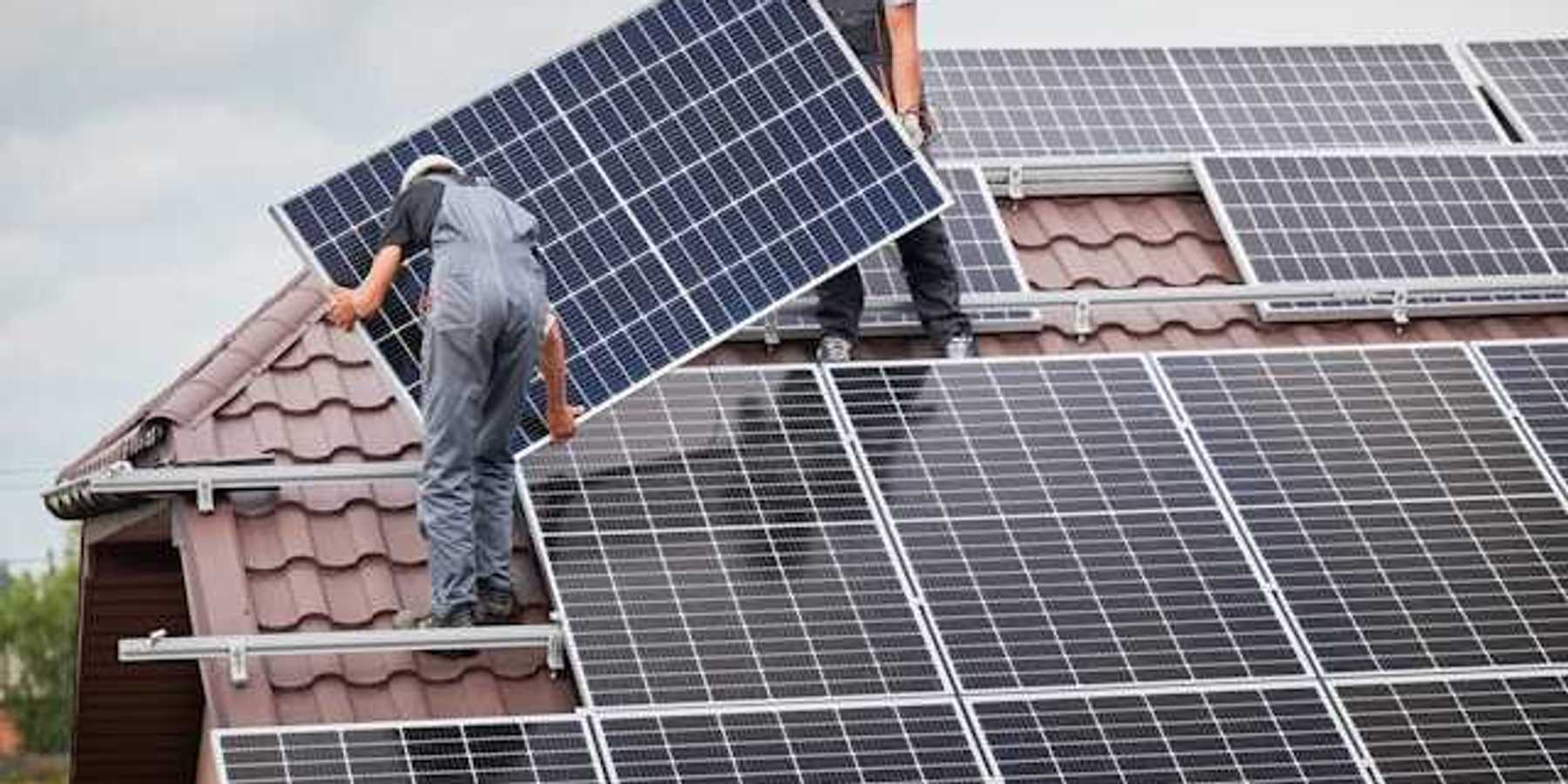 Two men on a roof with overalls on installing a solar panel
