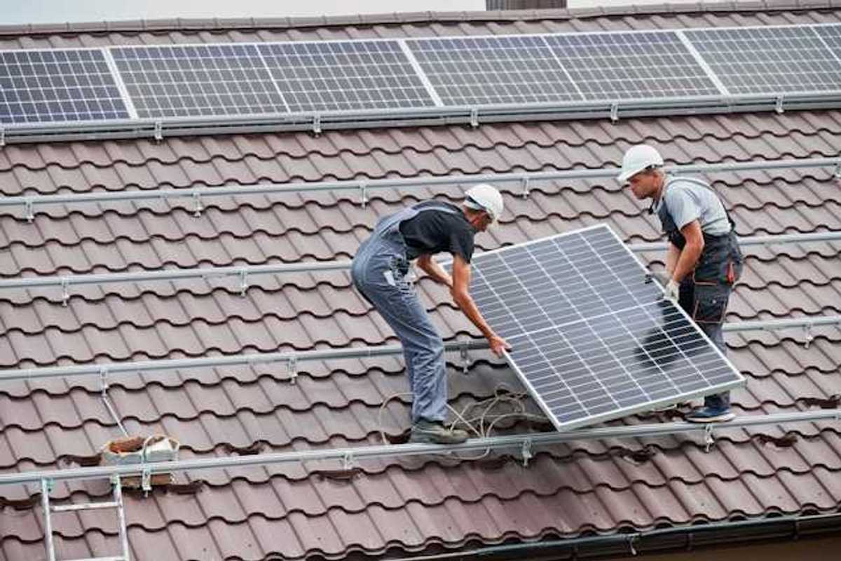 Two men placing solar panels on a red tiled roof