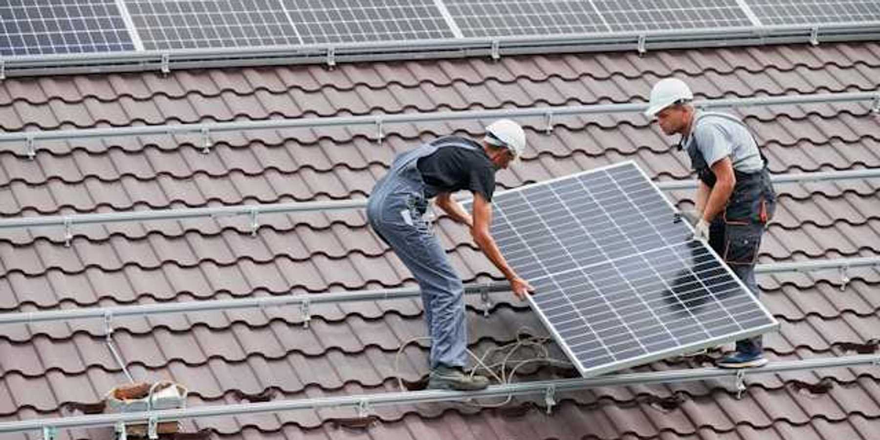 Two men placing solar panels on a red tiled roof