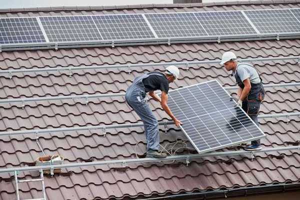 Two men placing solar panels on a red tiled roof