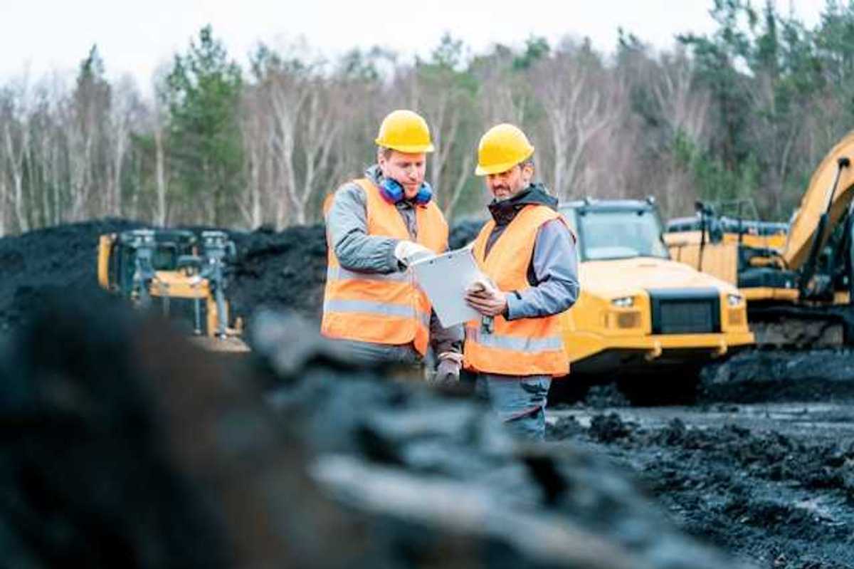 Two men wearing orange safety vests standing in front of piles of coal