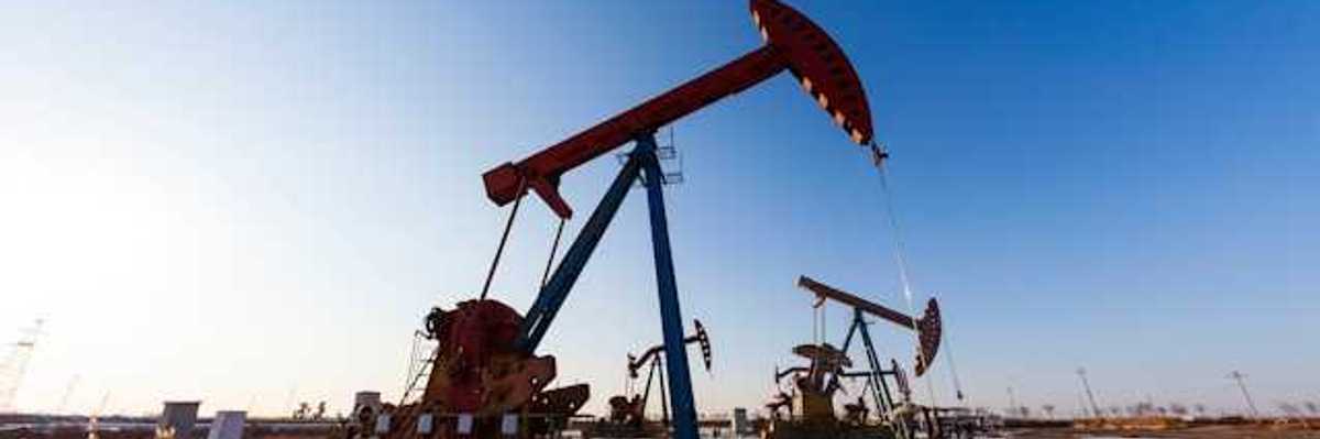 Two oil pump jacks in a snowy field under a blue sky