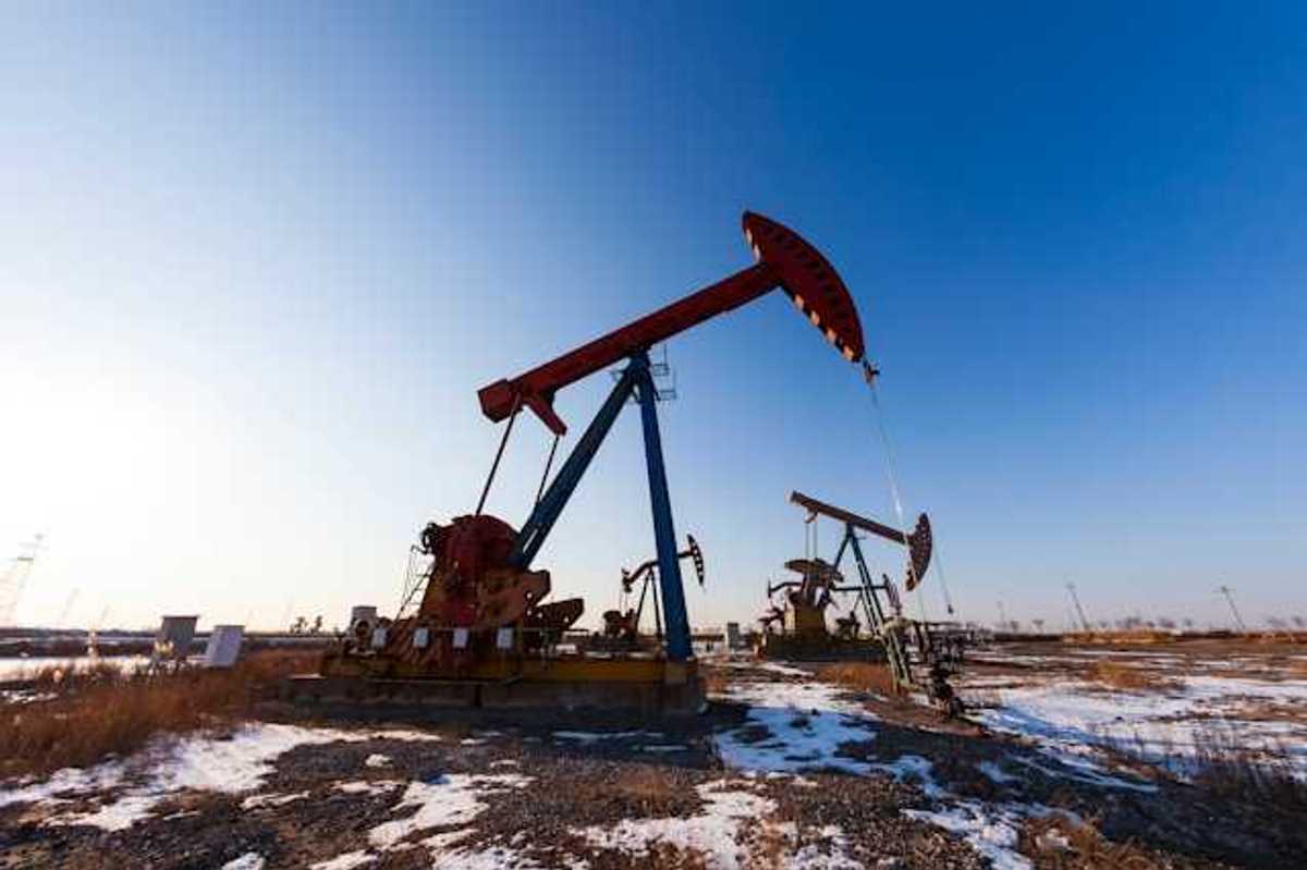 Two oil pump jacks in a snowy field under a blue sky