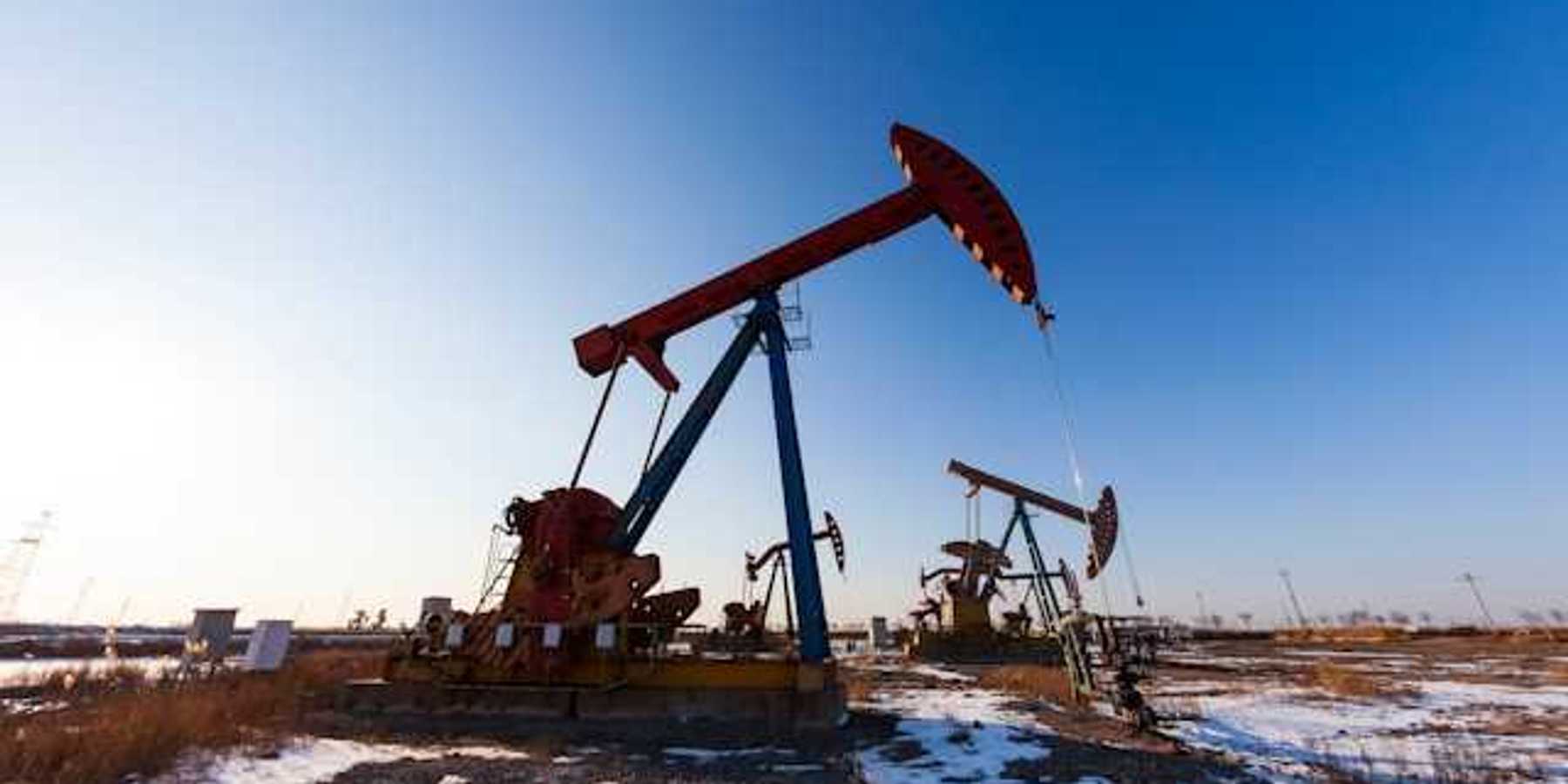 Two oil pump jacks in a snowy field under a blue sky