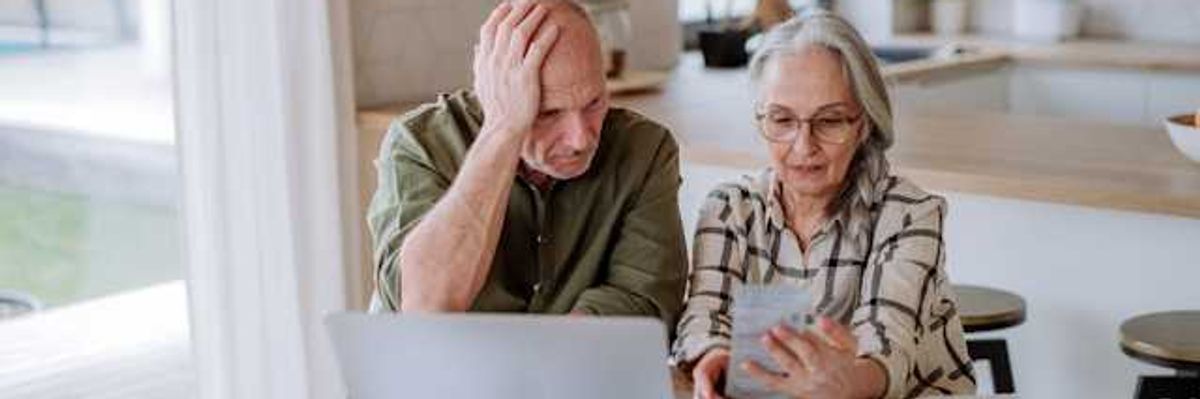 Two older people sitting at a kitchen table looking at bills