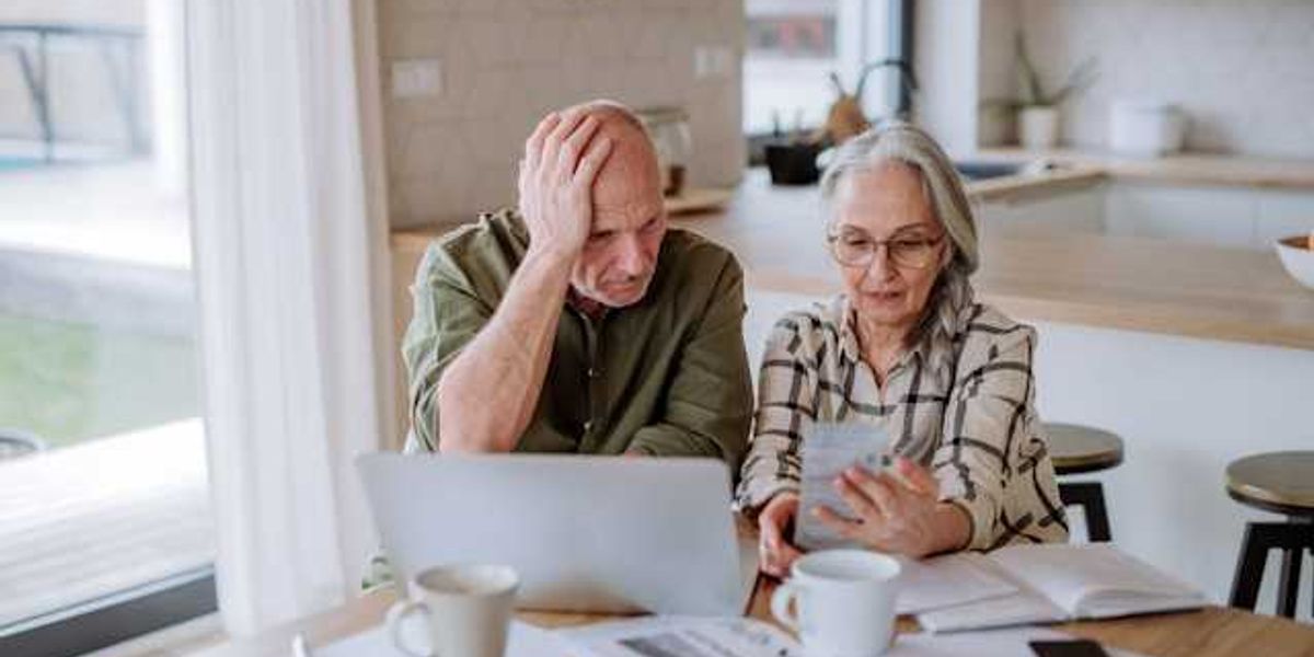 Two older people sitting at a kitchen table looking at bills
