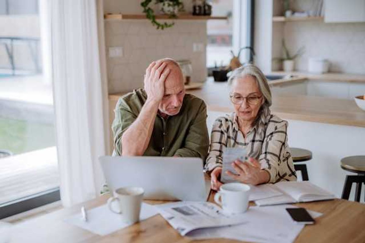 Two older people sitting at a kitchen table looking at bills