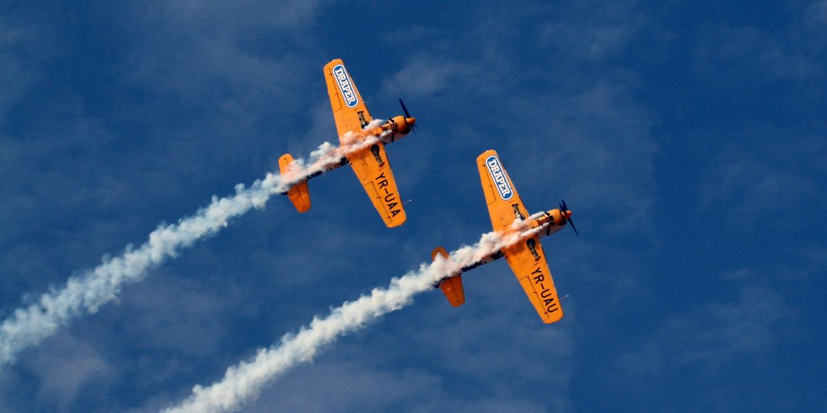 Two orange planes with trails of smoke behind them.