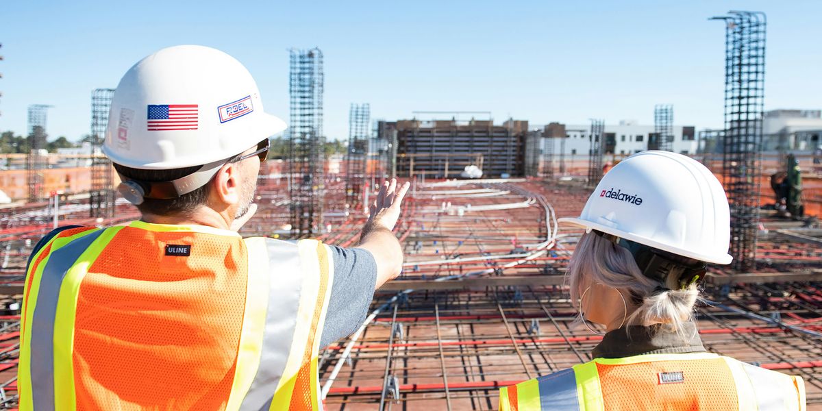 Two people in hard hats looking out over a building construction site.