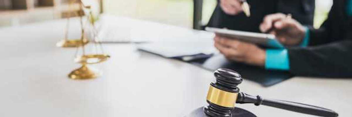 Two people looking at documents at a desk with the scales of justice and a wooden court gavel