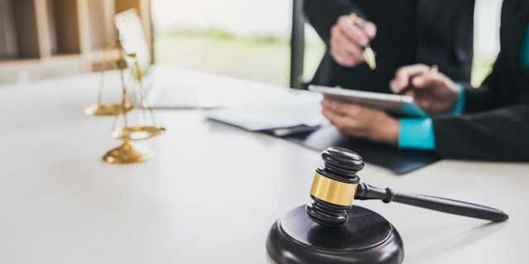 Two people looking at documents at a desk with the scales of justice and a wooden court gavel