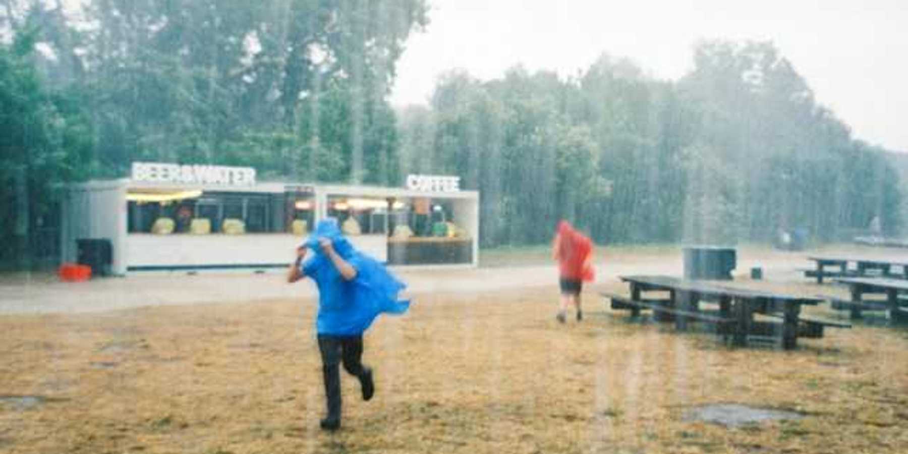 Two people running in the rain wearing ponchos outside of a drink stand