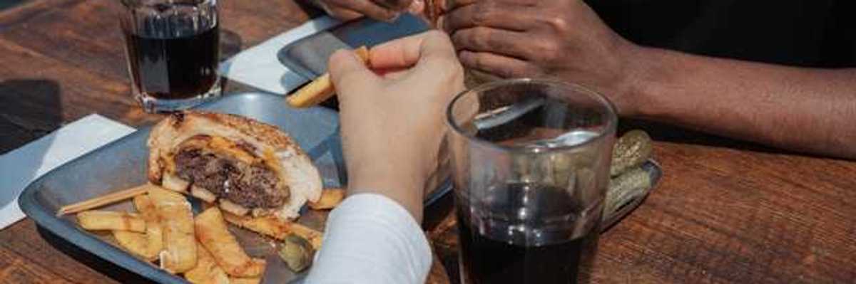 Two people's hands on a table with trays of burgers and coca cola in glasses