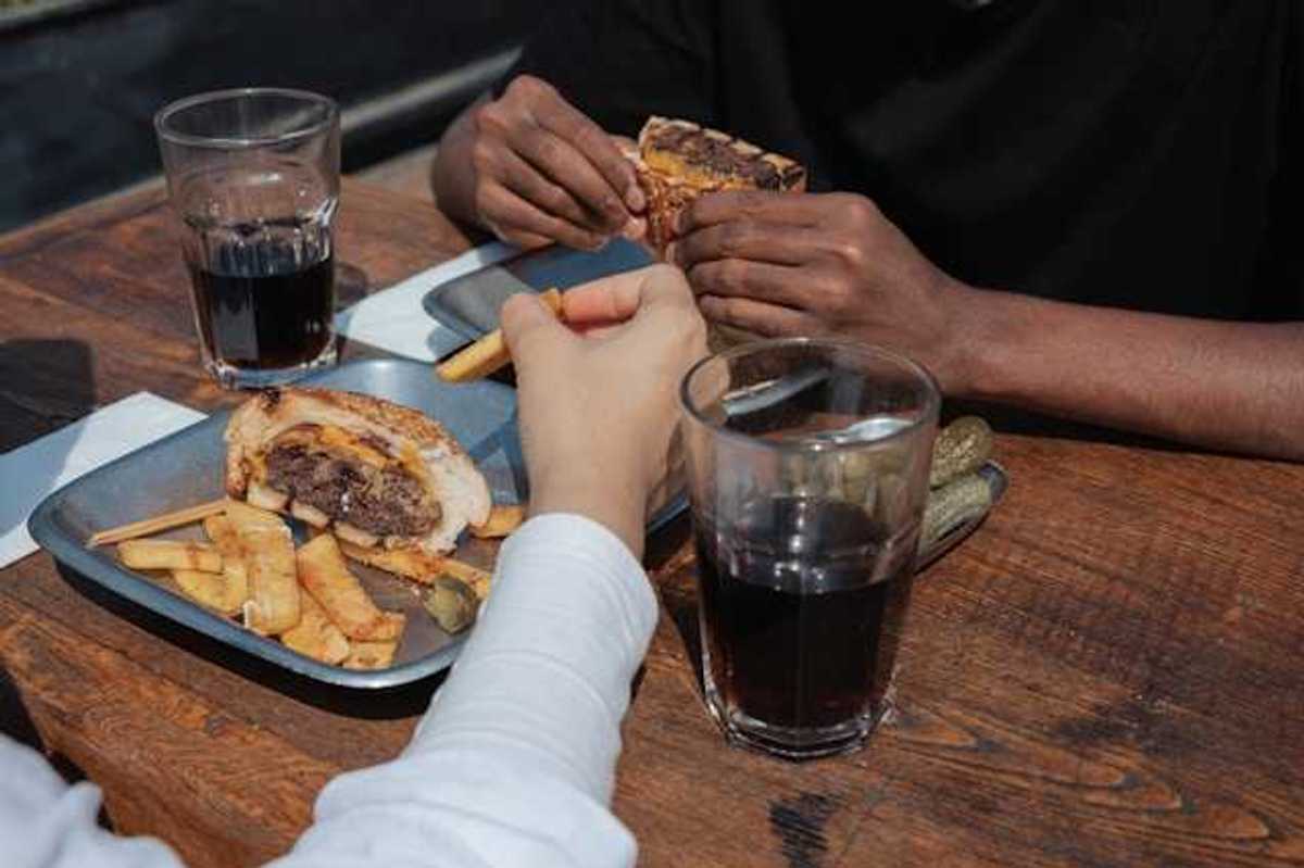 Two people's hands on a table with trays of burgers and coca cola in glasses