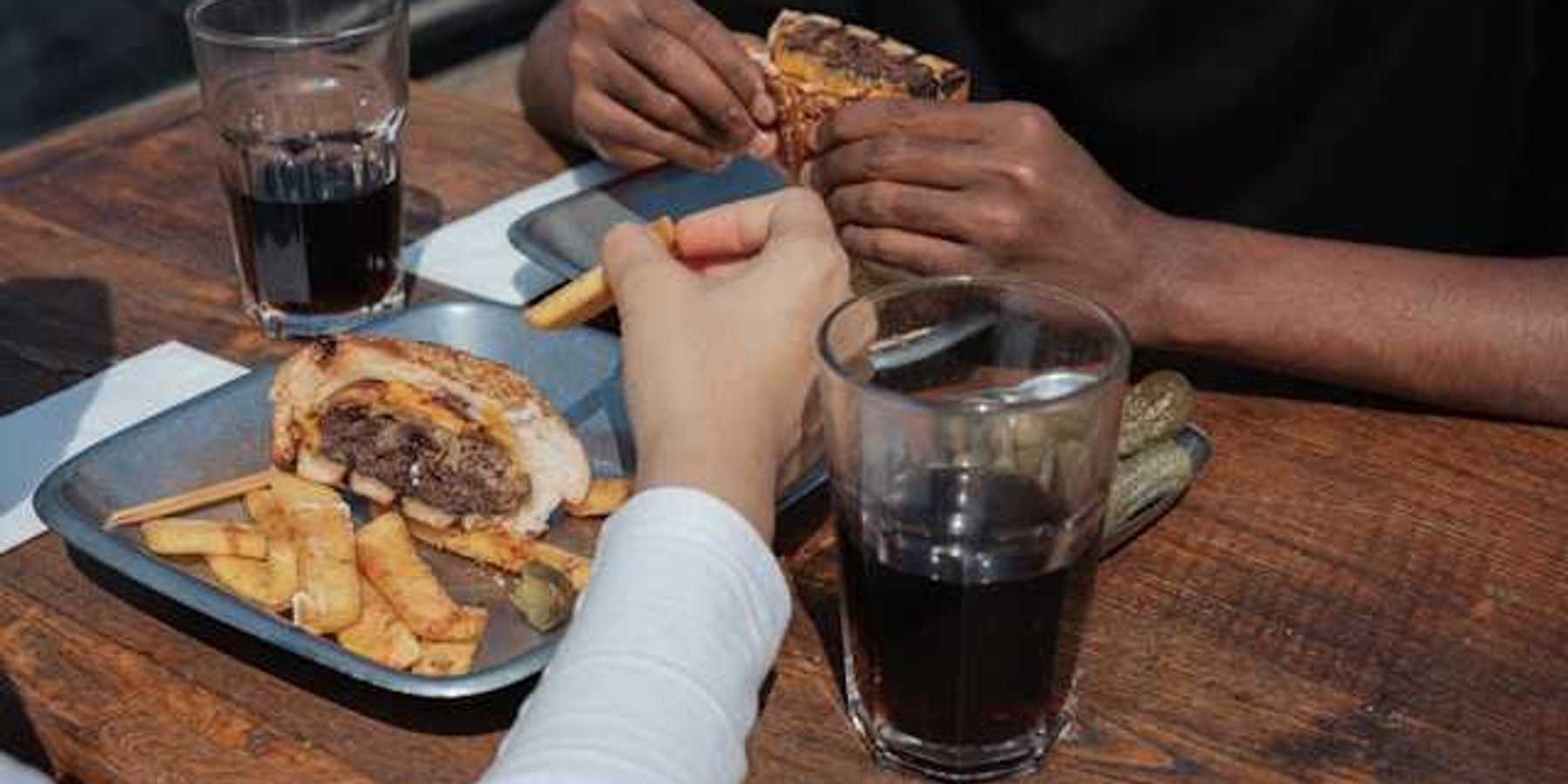 Two people's hands on a table with trays of burgers and coca cola in glasses