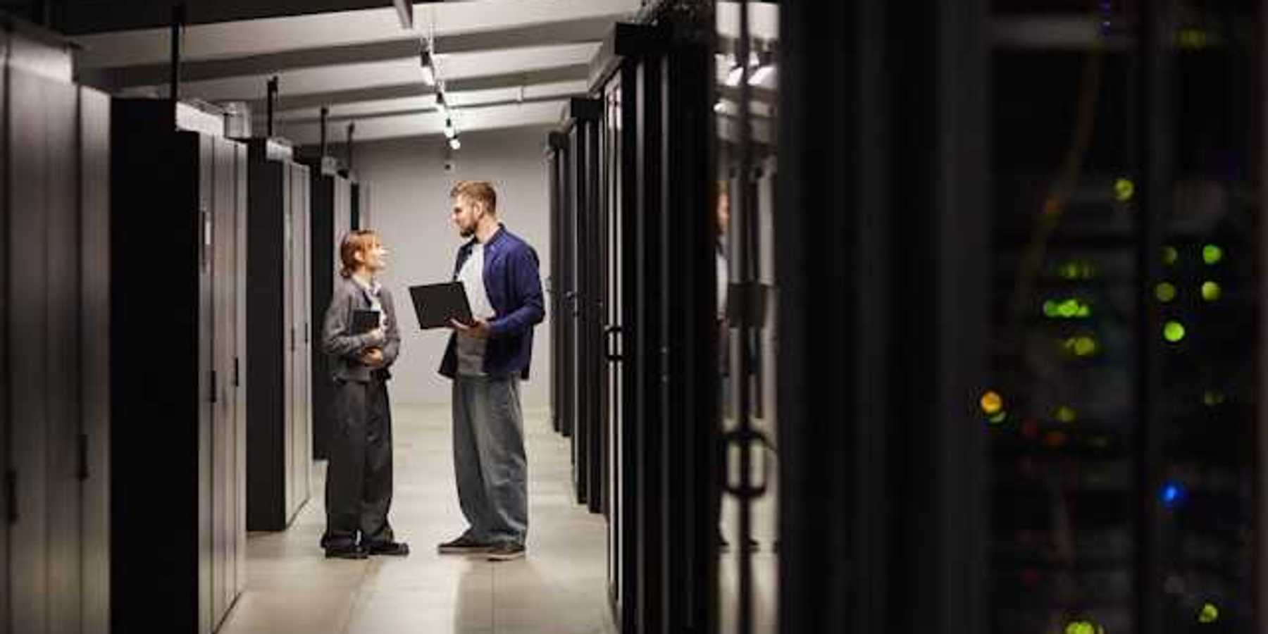 Two people standing and talking next to data servers in a data center