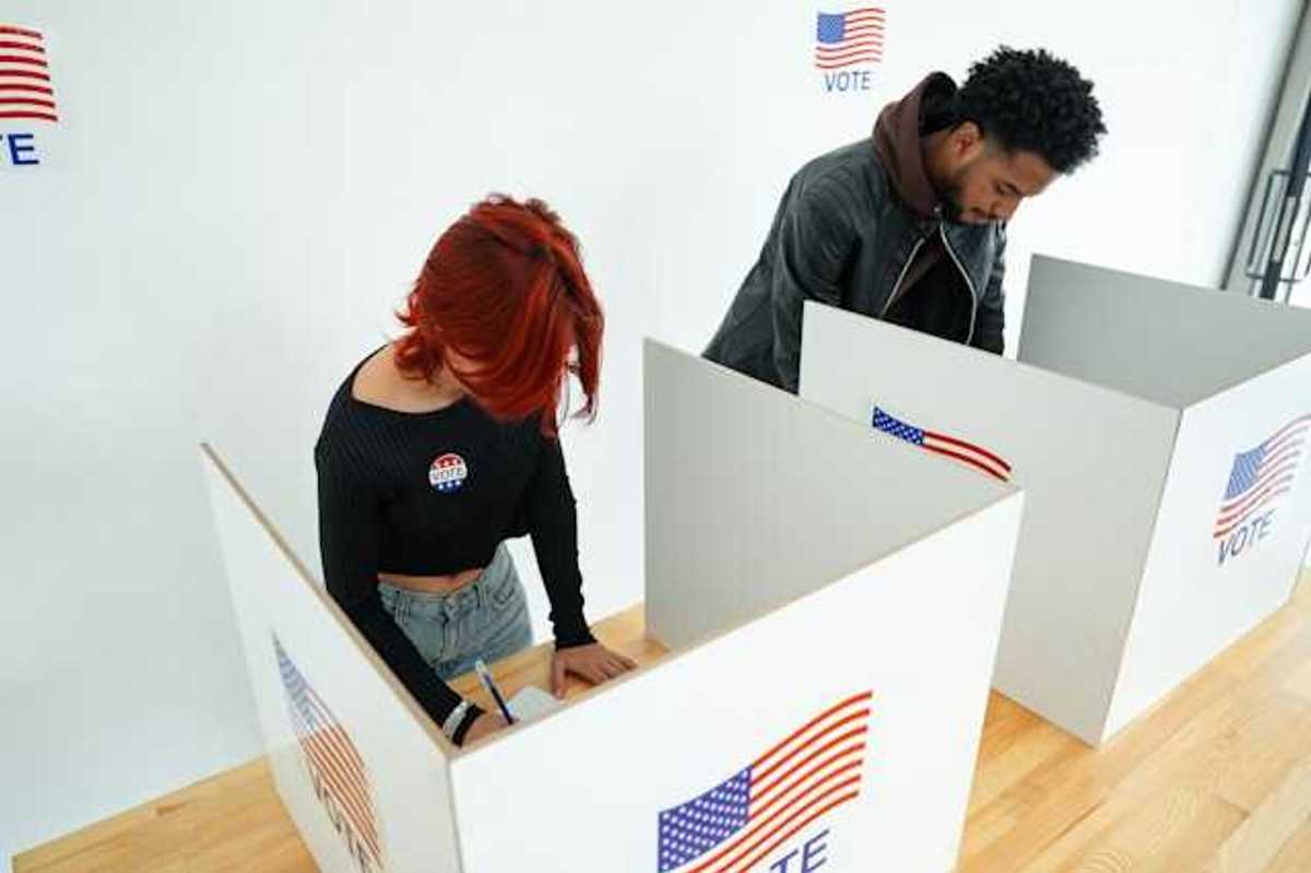 Two people standing at voting booths filling out ballots