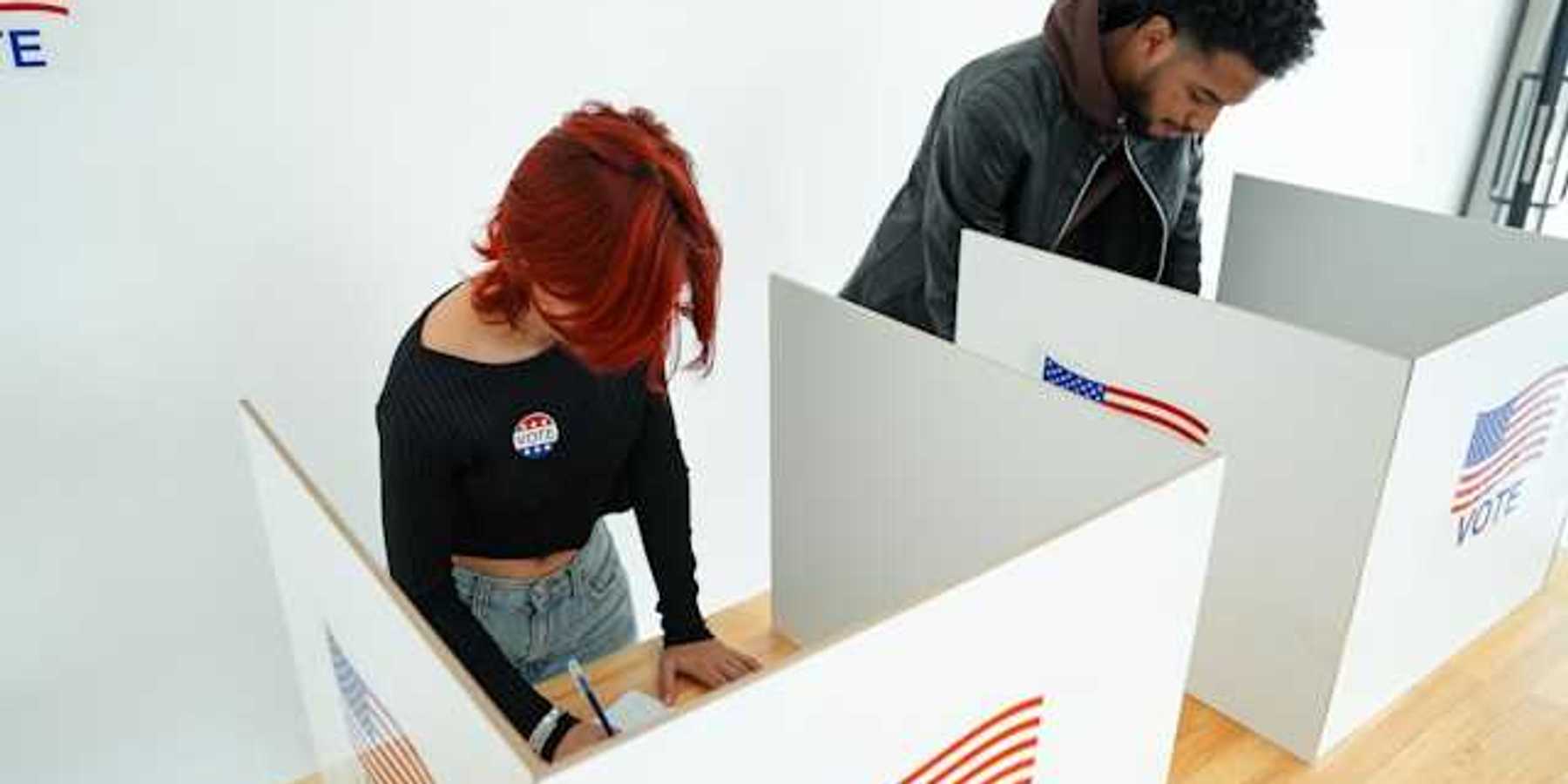 Two people standing at voting booths filling out ballots