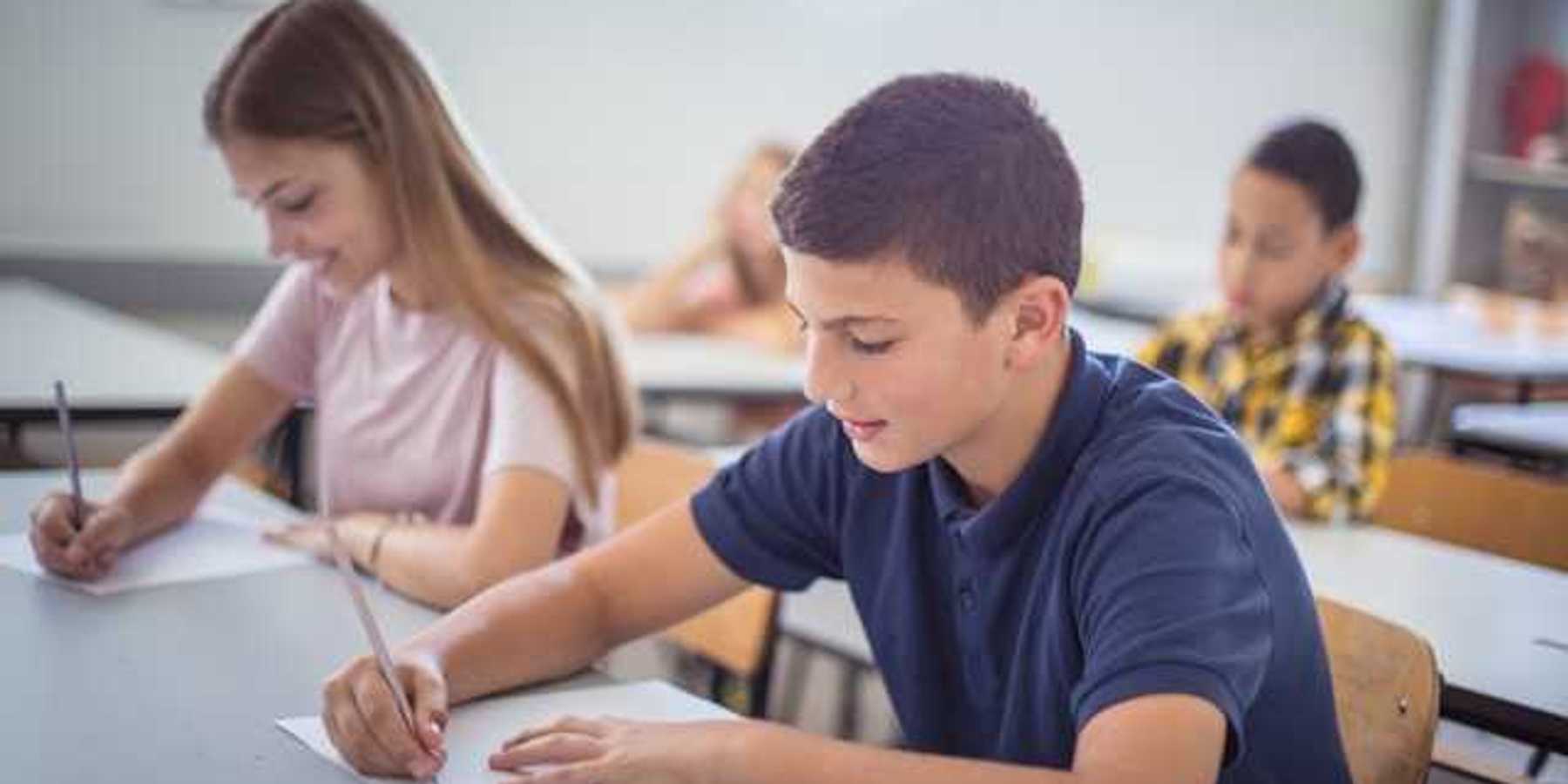 Two schoolchildren sitting at a desk in a classroom taking a test