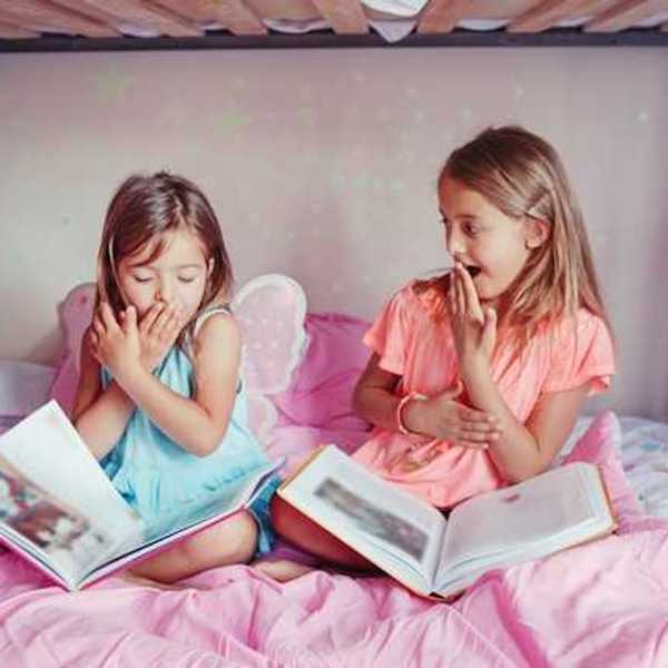 Two small girls sitting on a bed laughing with open books on their laps