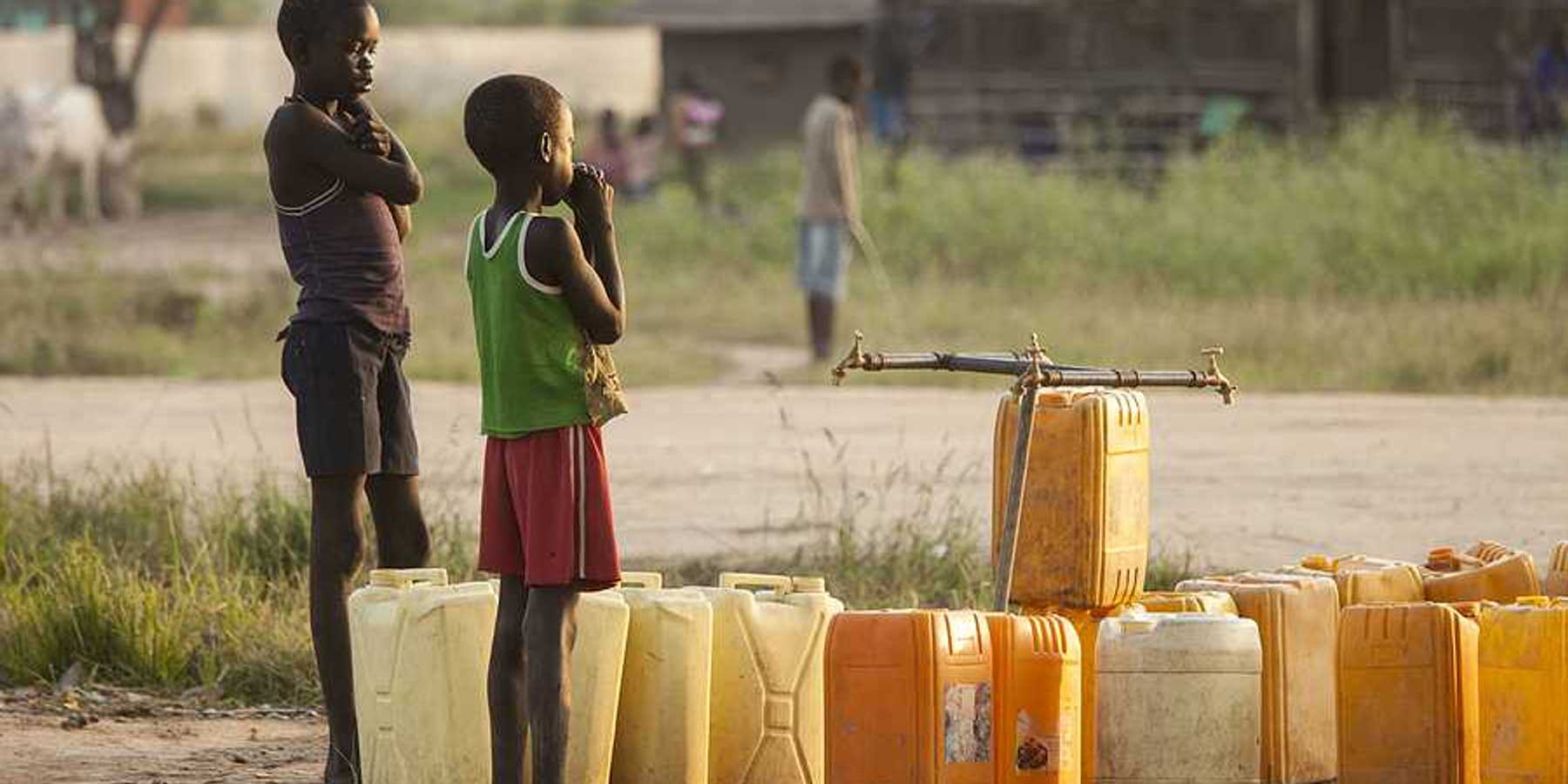 Two Sudanese children standing in a village next to plastic water jugs