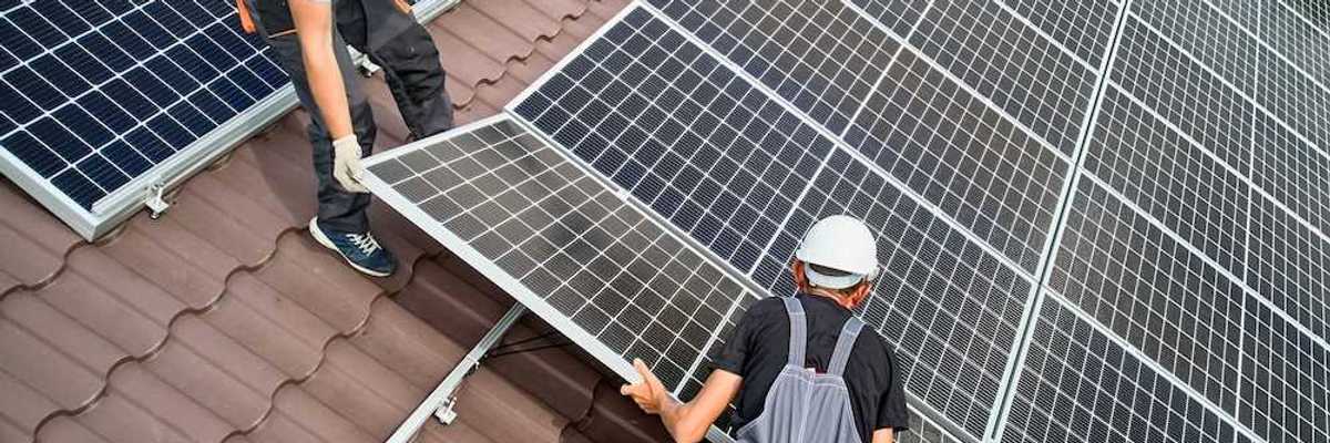 Two workers installing solar panels on a curved tile roof