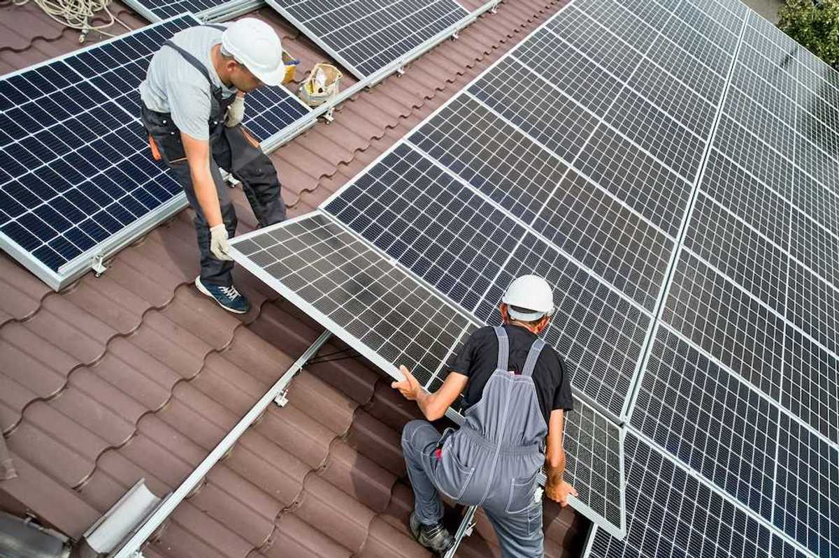 Two workers installing solar panels on a curved tile roof