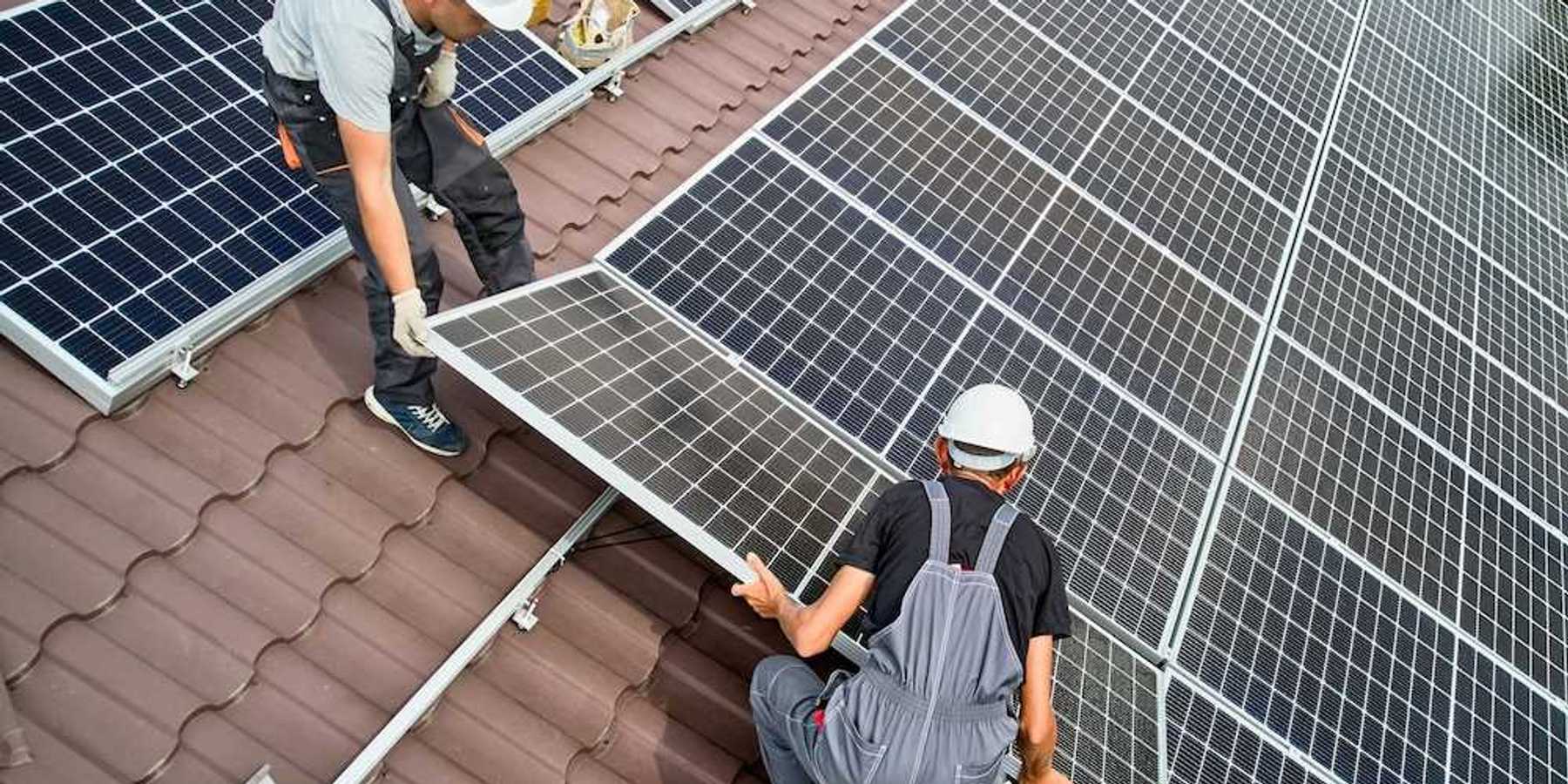 Two workers installing solar panels on a curved tile roof