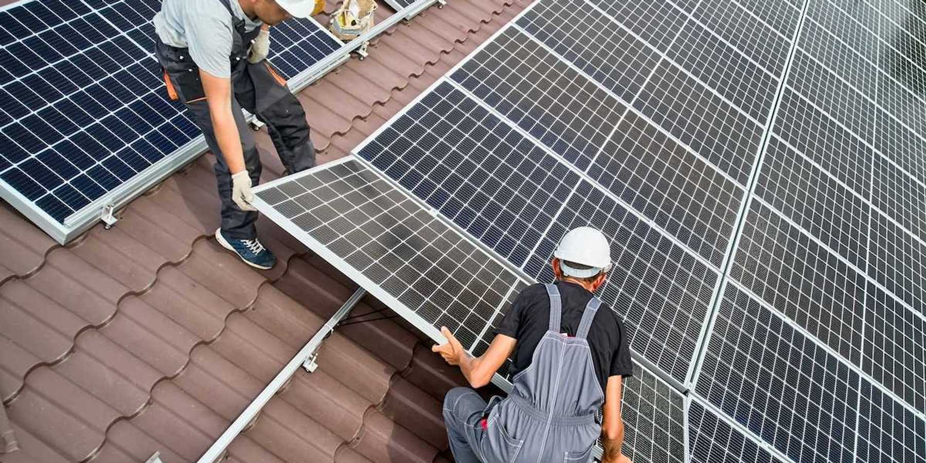 Two workmen installing solar panels on a rooftop