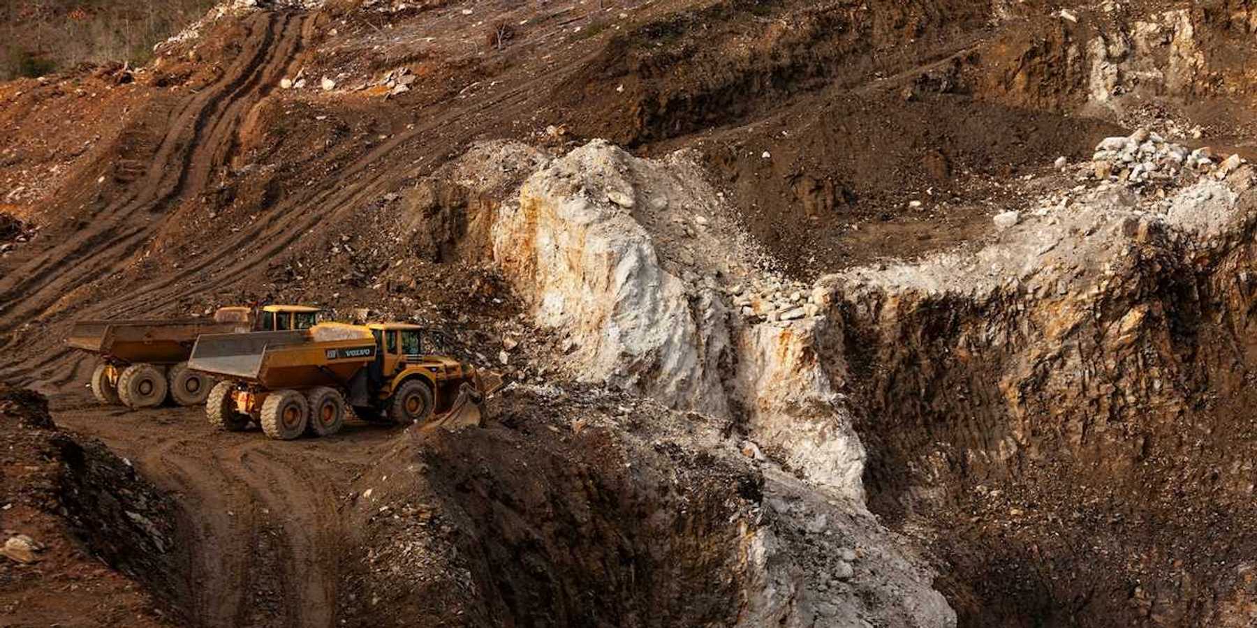 Two yellow "rock trucks" parked at a mining cut, surrounded by disturbed earth and mining