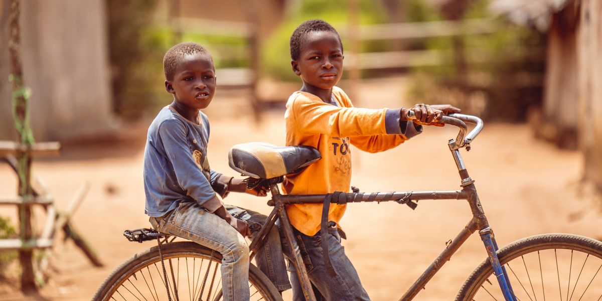 two young African boys sitting on top of an old bike.