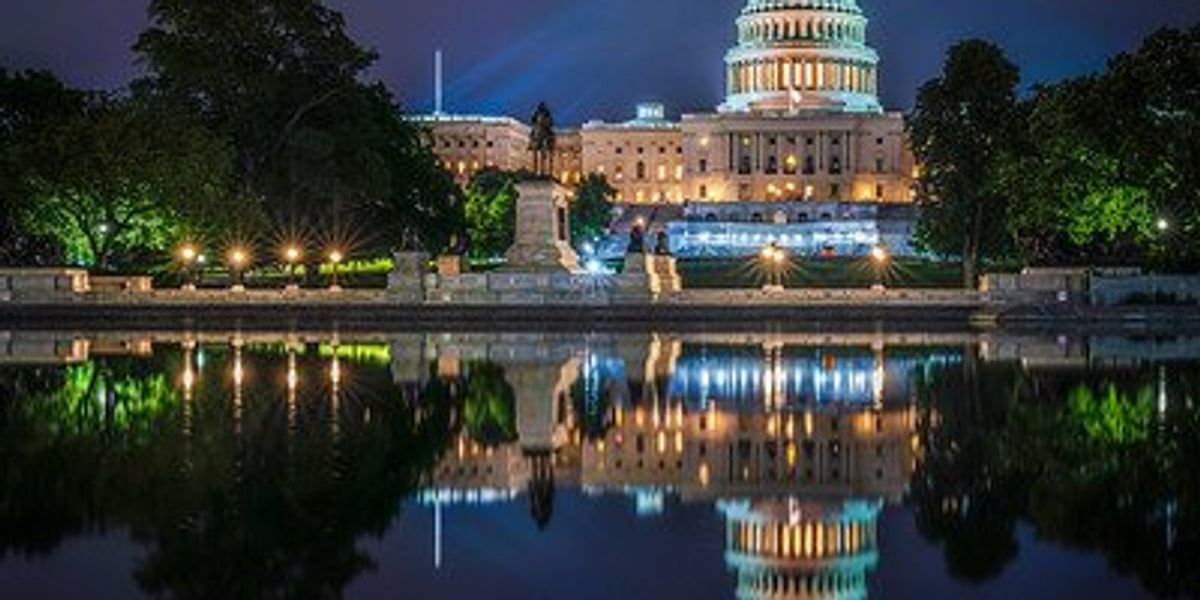 U.S. Capitol building illuminated at night, reflected in a pool of water in the foreground.