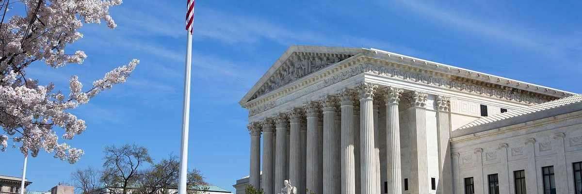 United States Supreme Court building and grounds with US Flag and cherry blossoms on tree.