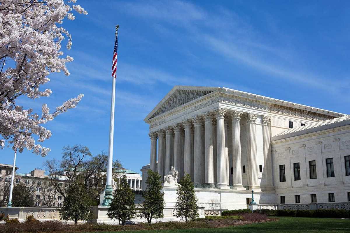 United States Supreme Court building and grounds with US Flag and cherry blossoms on tree.