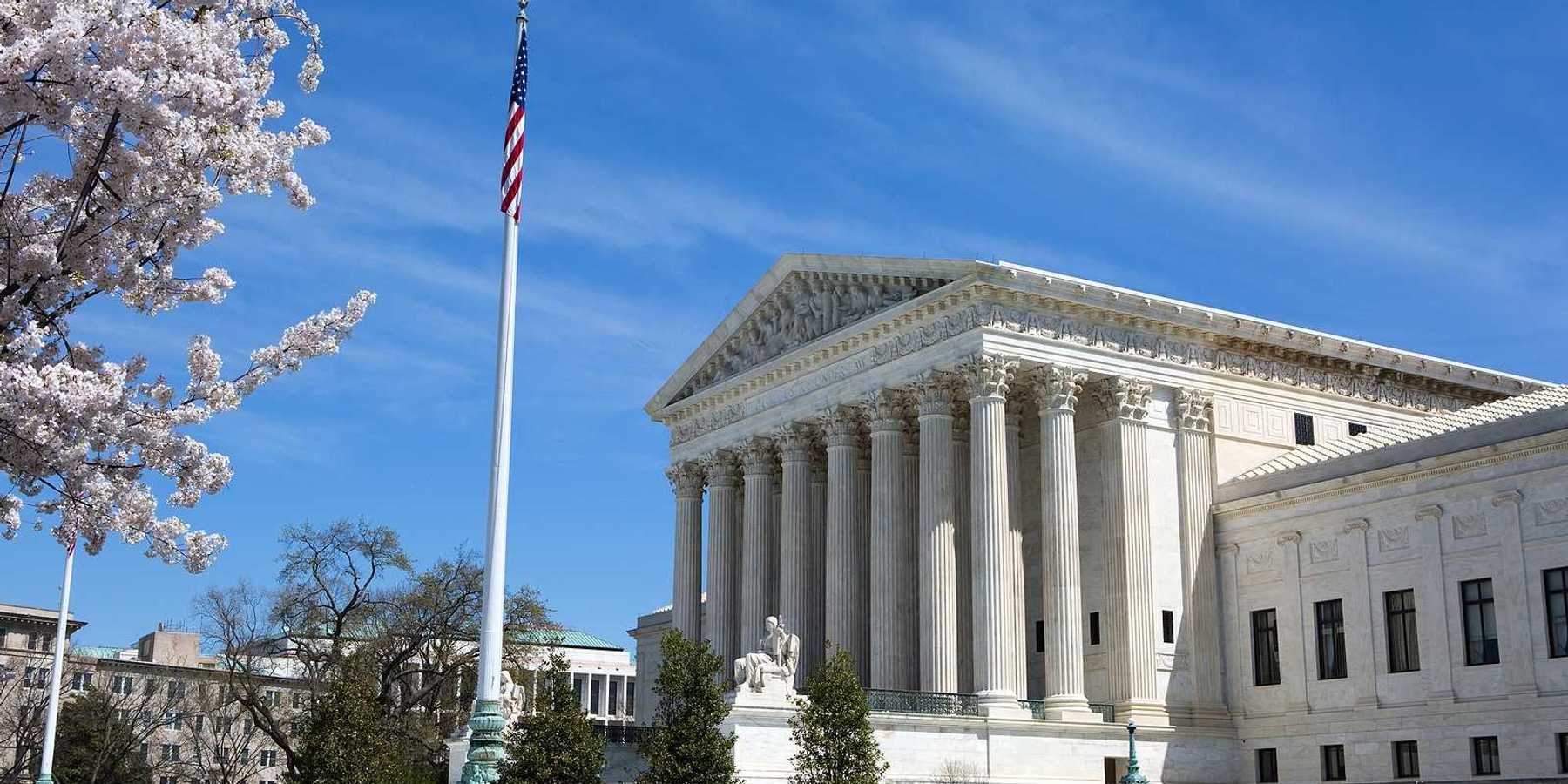 United States Supreme Court building and grounds with US Flag and cherry blossoms on tree.