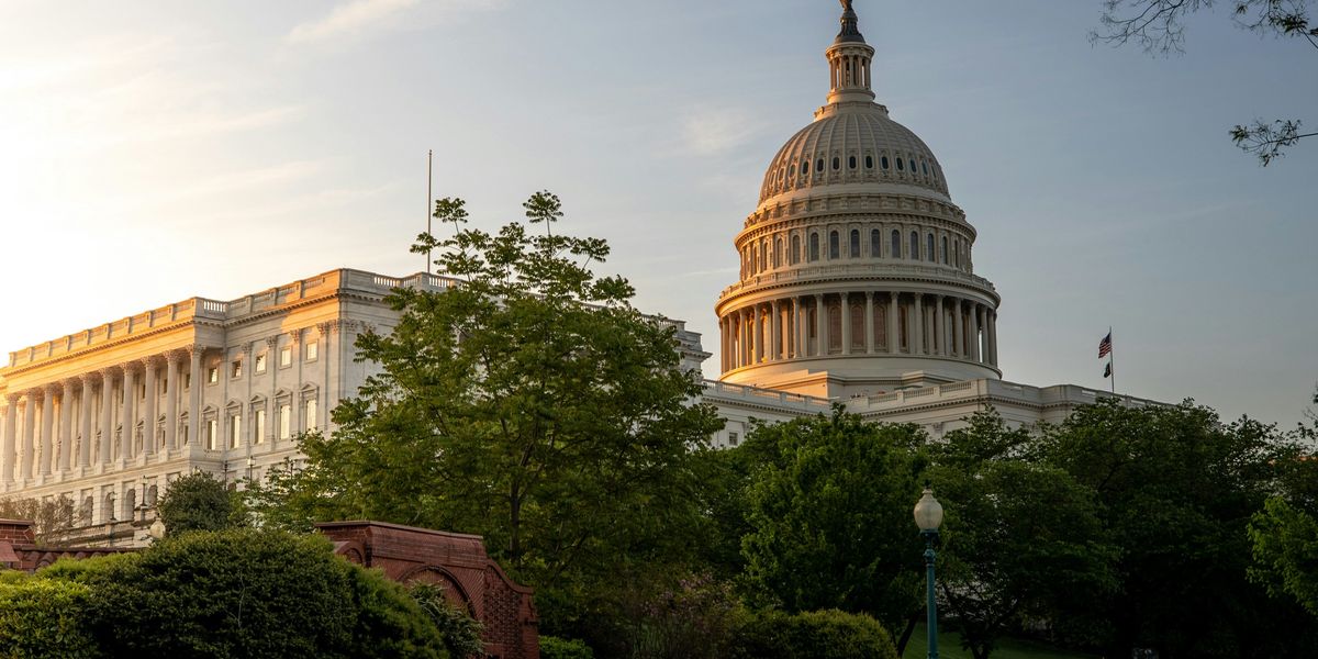 US Capitol dome touched by early morning sun with trees and a path in foreground.