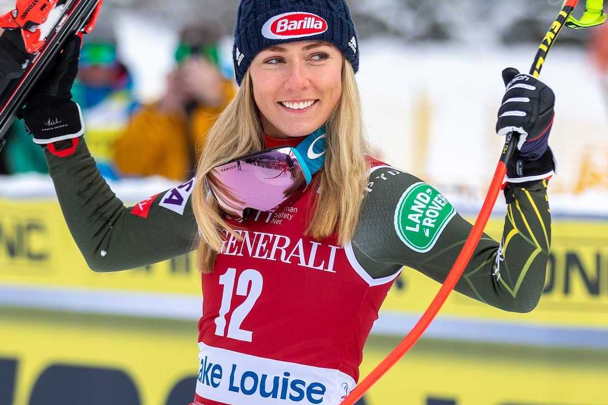 US skier Michaela Shiffrin in red bib holding skis and pole at finish