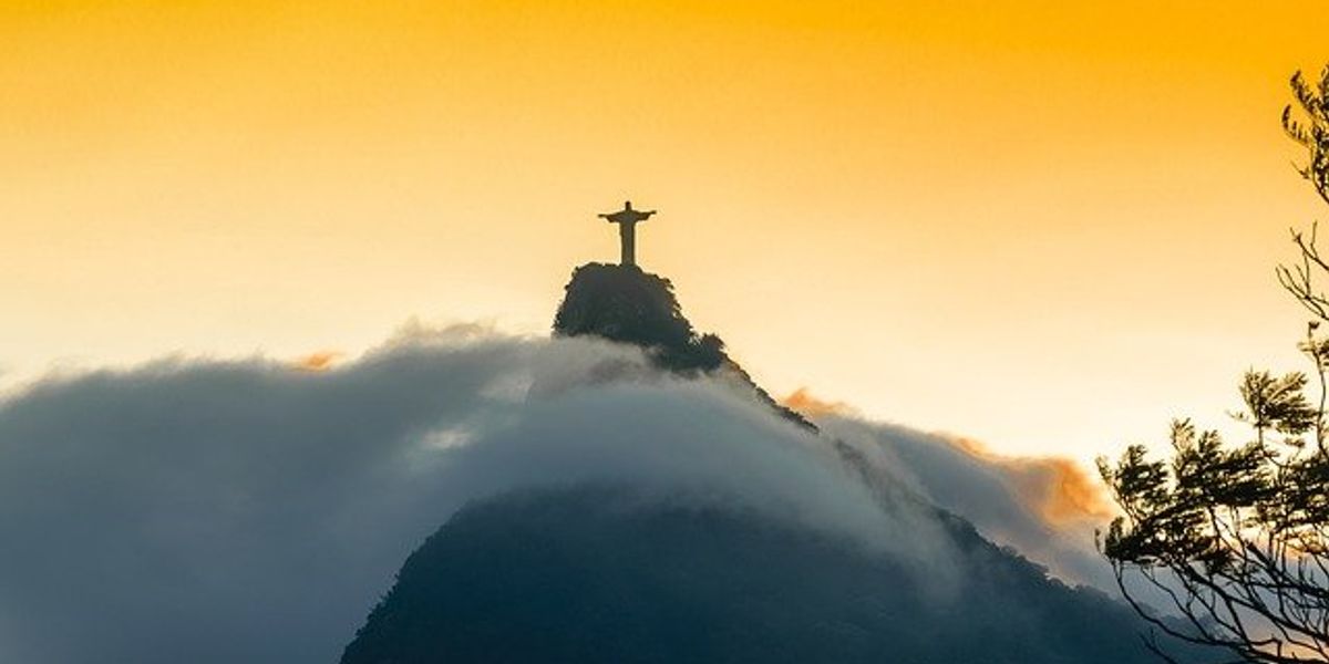 View of Christ the Redeemer statue in Rio de Janeiro on a mountain shrouded in mist with a yellow dawn sky.