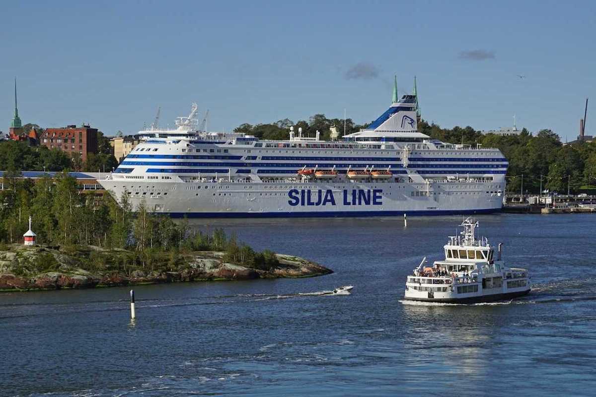 View of Helsinki harbor on a summer day with the Suomenlinna fortress ferry in the front and a large ferry ship behind it.