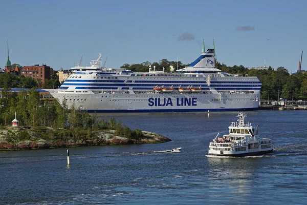 View of Helsinki harbor on a summer day with the Suomenlinna fortress ferry in the front and a large ferry ship behind it.